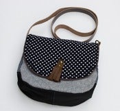 Image of a small cross body bag with a black + white polka dot flap